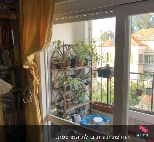 חלון זכוכית עם וילון צהוב, צמחים על מדף בחוץ.